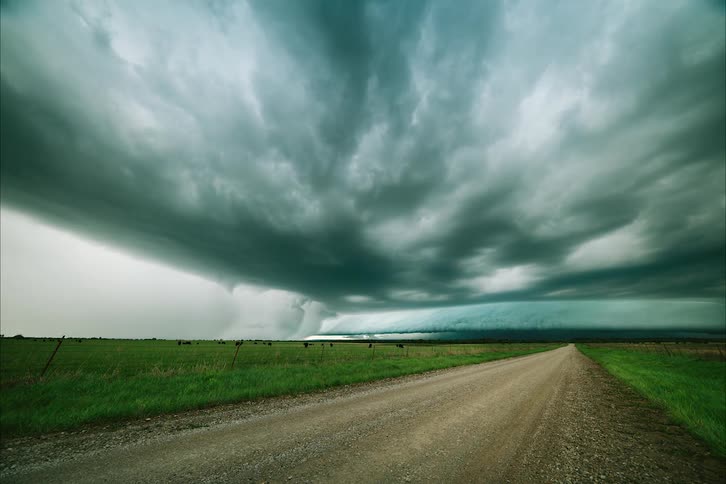 Time lapse of storm clouds rolling a dirt road next to a field on the countryside