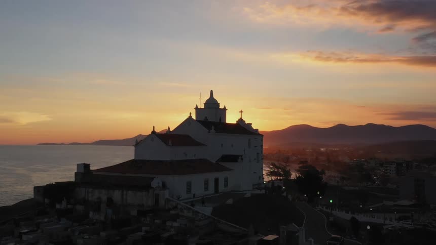 Birds fly around the church by the shore during sunset