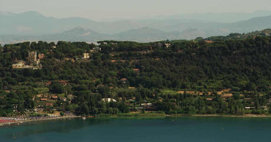 A small village on a green hillside with a serene lake in front and mountain ridge behind