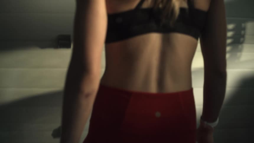 Young woman wearing fitness clothing approaching a barbell on the floor to lift it