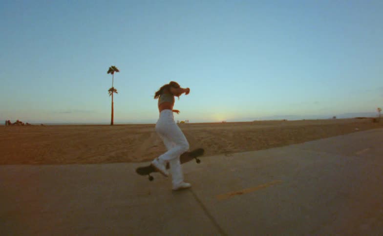 Young woman rides a skateboard on a road in the beach next to the ocean caught on vintage film