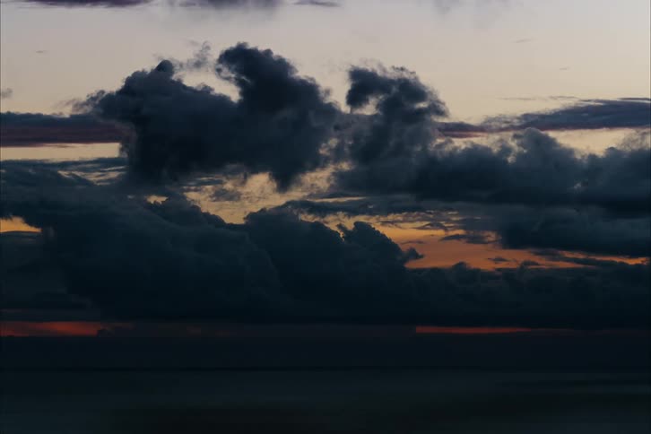 Dark clouds move over the coast as the sun sets