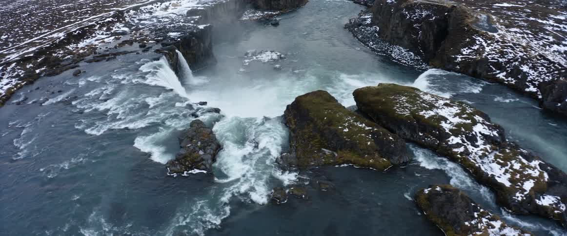 Water flows over cliff in several waterfalls near snow dappled terrain