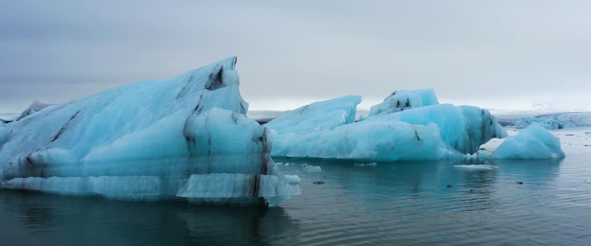 Water rippling around blue icebergs on a cloudy day