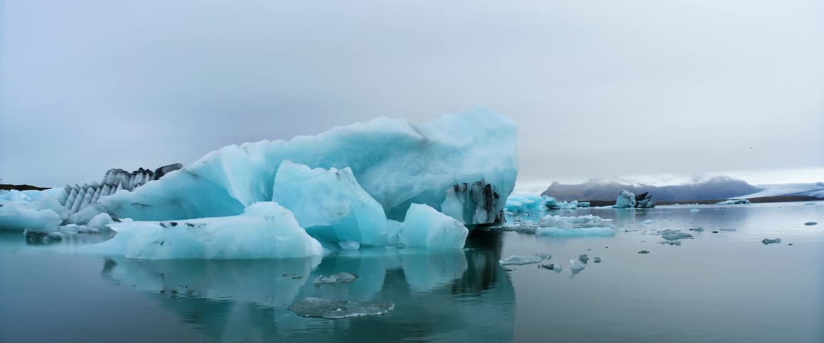 Icebergs and chunks of ice float in the ocean under a cloudy sky