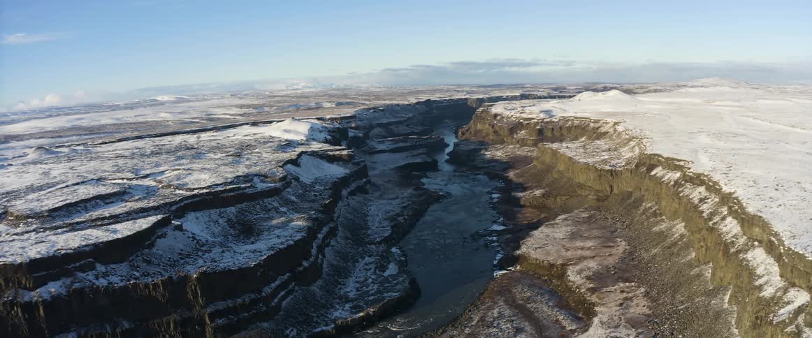 An aerial view of a river flowing through a snowy canyon in winter