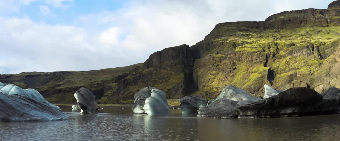 Ice floats in water near promontory under a cloudy sky