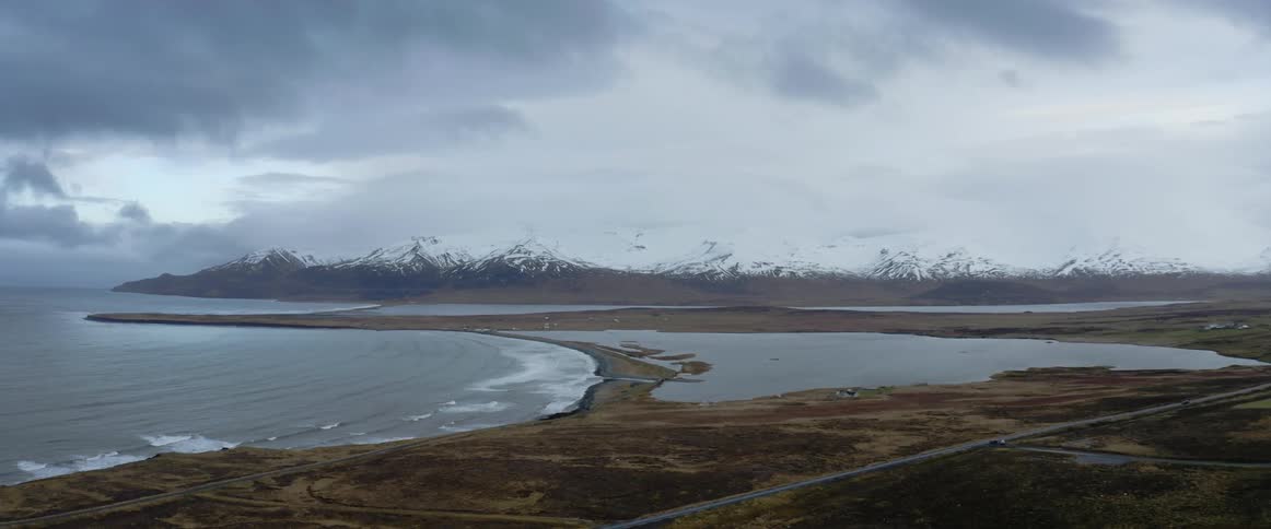 Aerial view of a bay in the coast next to the snow covered peaks of a mountain range