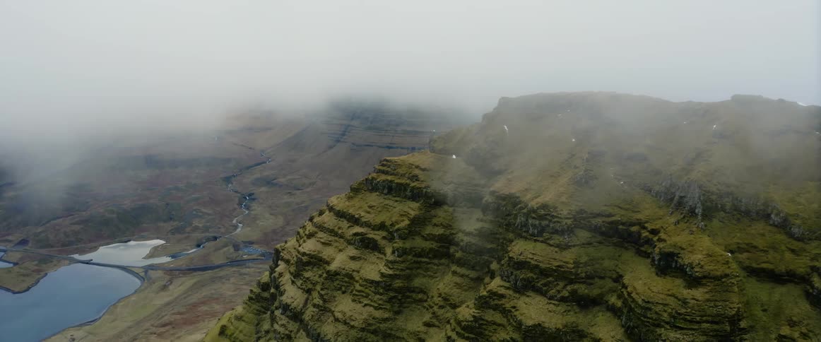 Low lying clouds cover top of terraced cliffs near reflective lakes