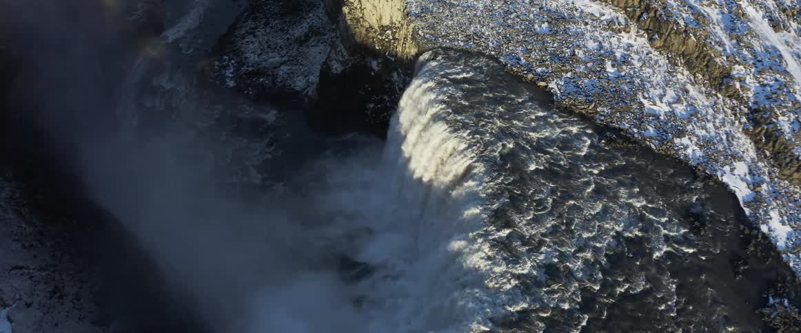 A waterfall flows down a cliff splashing and flowing into the river below