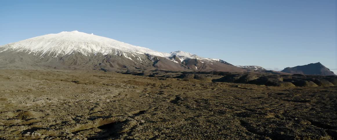 A large ice covered volcano rises high above other mountains