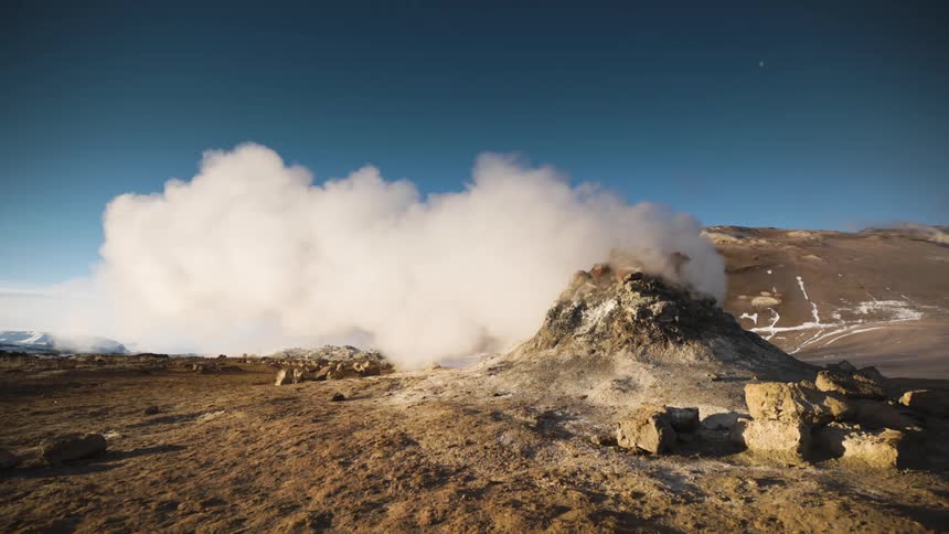 Steam rises from mound and flows toward snowy horizon under a deep blue sky