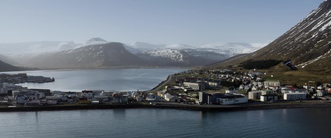 A coastal town on a peninsula at the base of a hill with mountains behind