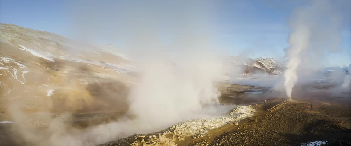 People standing watching smoke and steam billowing out of geysers