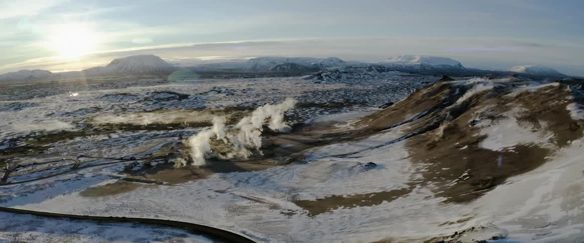 An aerial view of a snowy mountain landscape with steam pillars