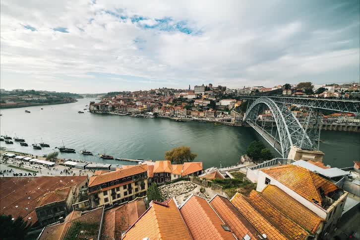 Traffic crosses both levels of the bridge and boats move through the river as people move along on the waterfront