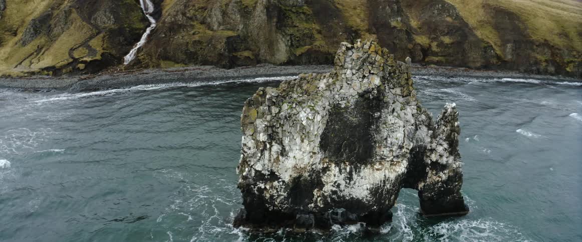An aerial view of ocean waves crashing into a large rock formation