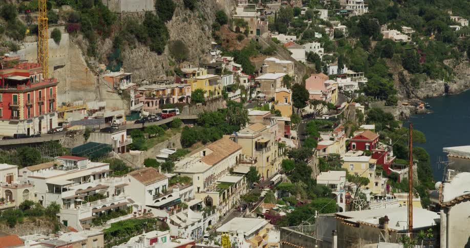 Vehicles driving on the narrow streets of a village built on the slopes of a coastal mountain