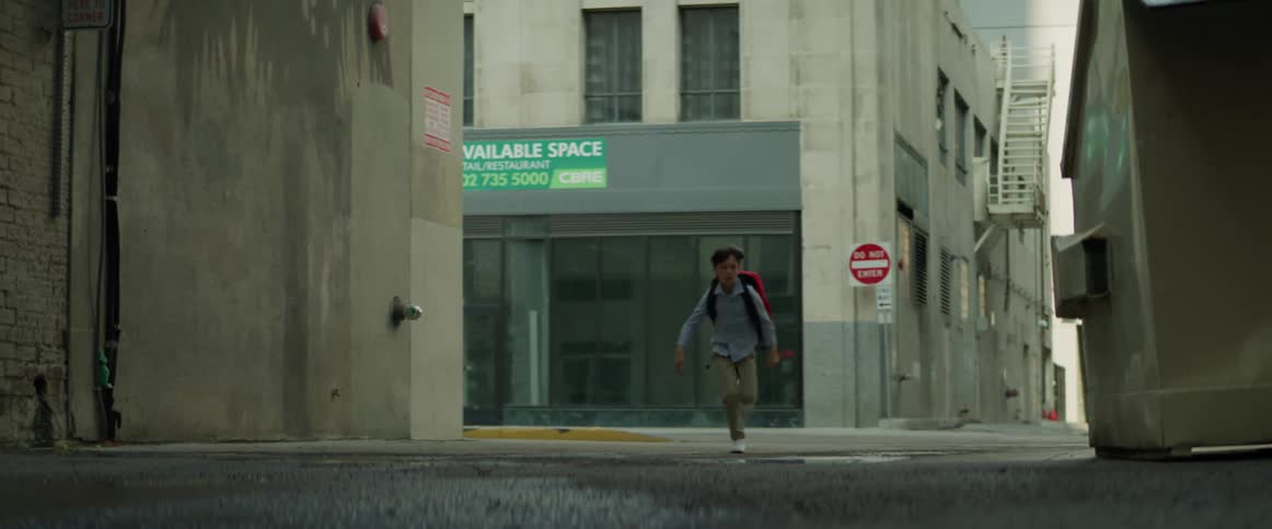Young boy carrying a red backpack running down an alleyway in the city