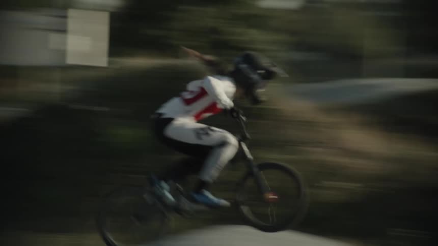 Young girl pedaling a motocross bike at full speed through the slopes of a track