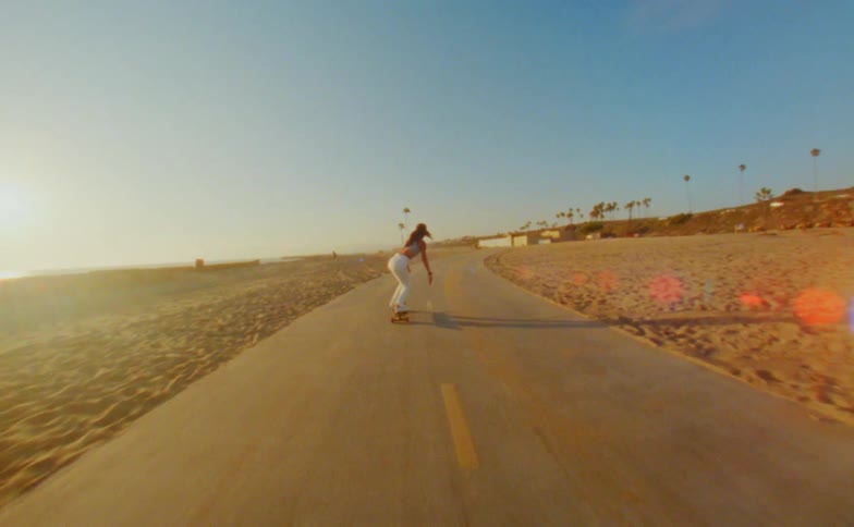 Young woman rides a skateboard on a road in the beach next to the ocean caught on vintage film