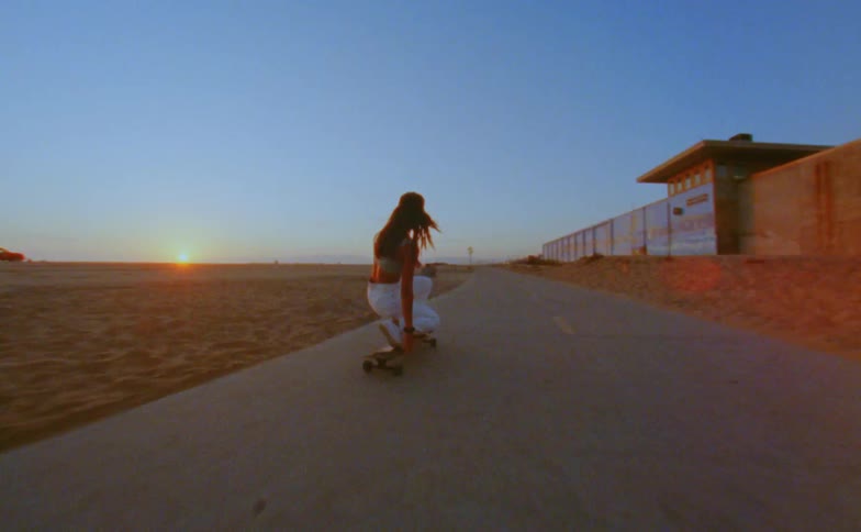 A woman rides a long board skateboard on a path near the beach sand