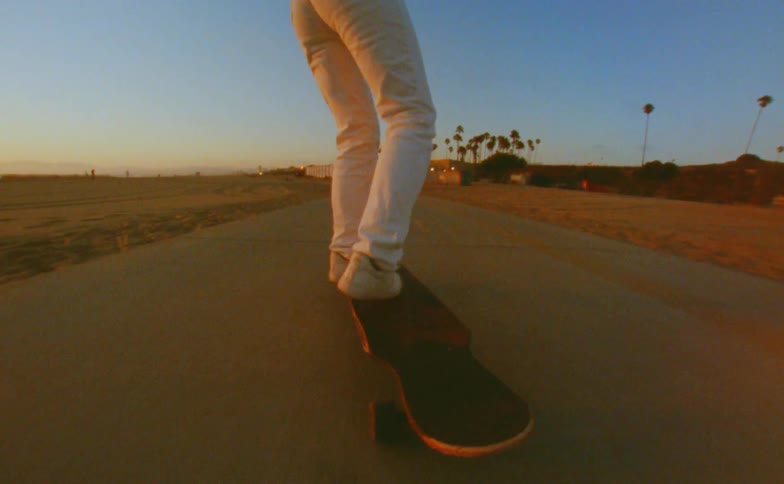 A woman walks forward on the skateboard deck as she rides on a path at the beach