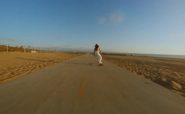 Young woman rides a skateboard on a road in the beach next to the ocean