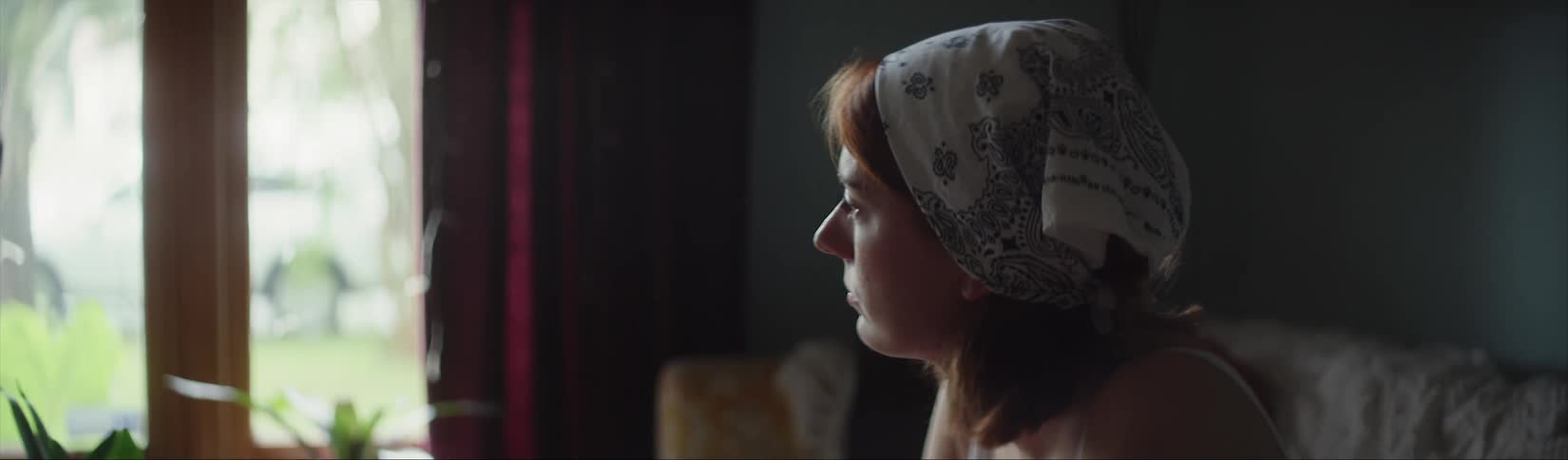 A woman wearing a kerchief on her head sitting on the couch looking out the window