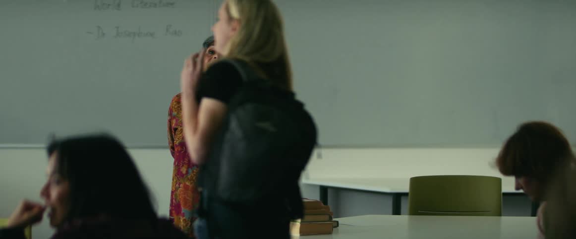 College students enter classroom with teacher standing in front of whiteboard