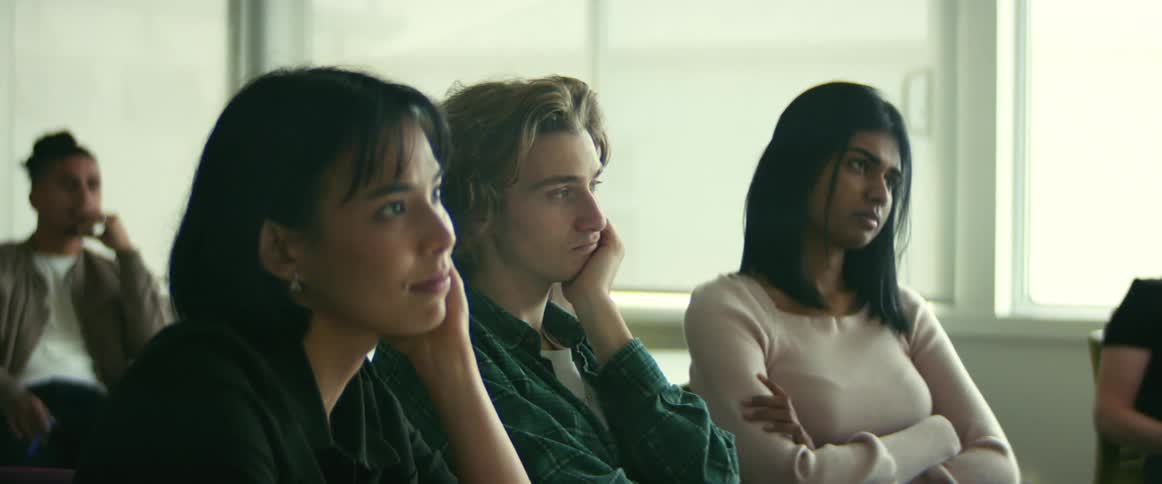 Students sitting at the table in the classroom listening to the teacher speak