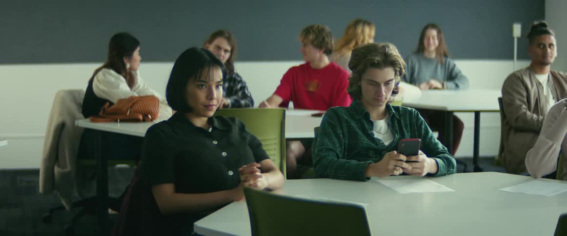 Students sit at tables while one checks their phone