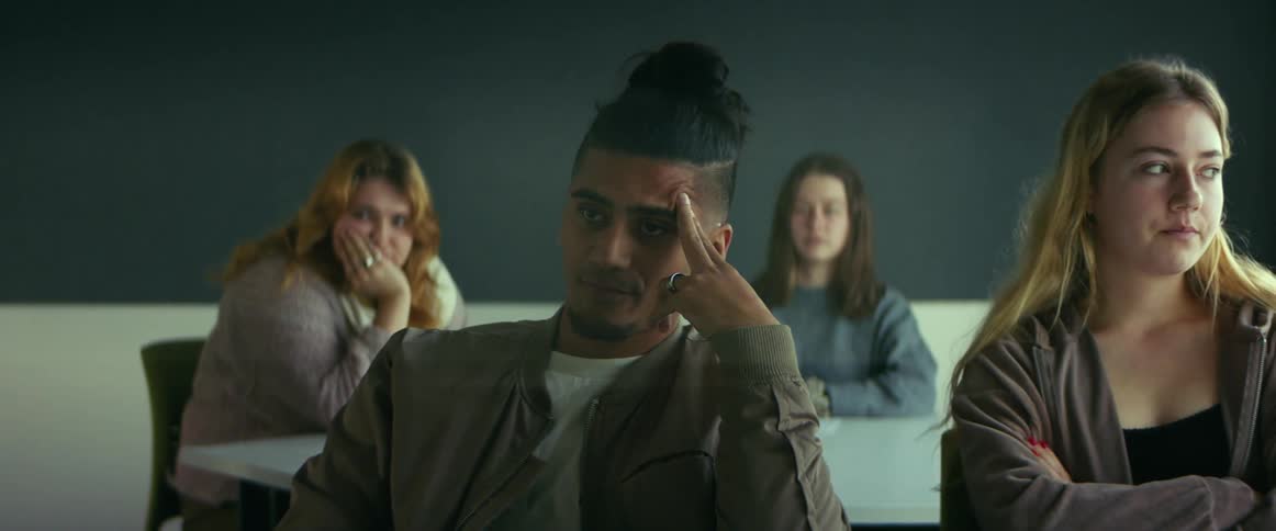 Bored man sitting at the table watching a class with other students in the classroom