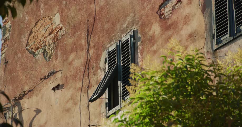 The side of a building in poor condition shows bent shutters large holes and general deterioration