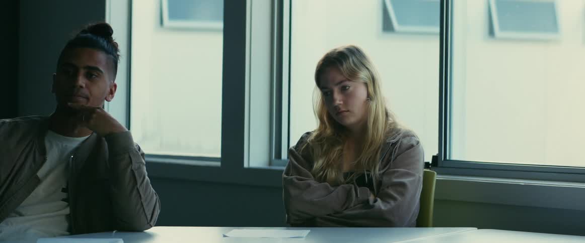 A man and woman sit in a room at a table looking worried and despondent as if they are anticipating something negative