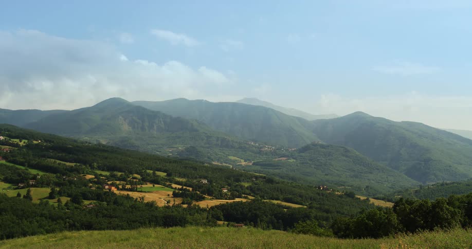 Farms and fields on the gentle slopes of the hills next to the mountains under a blue sky