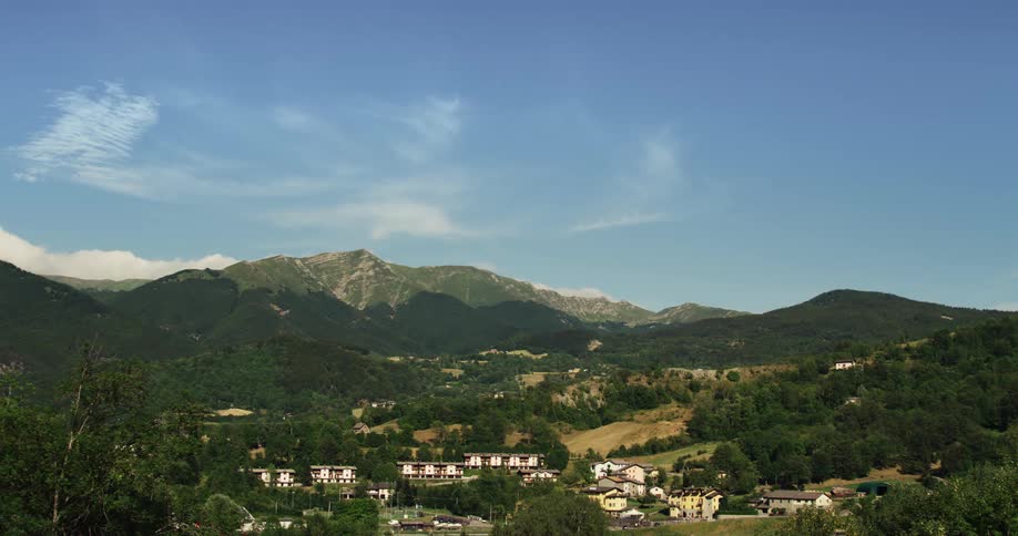 Homes and buildings in a small town on green hills at the base of a mountain under a blue sky