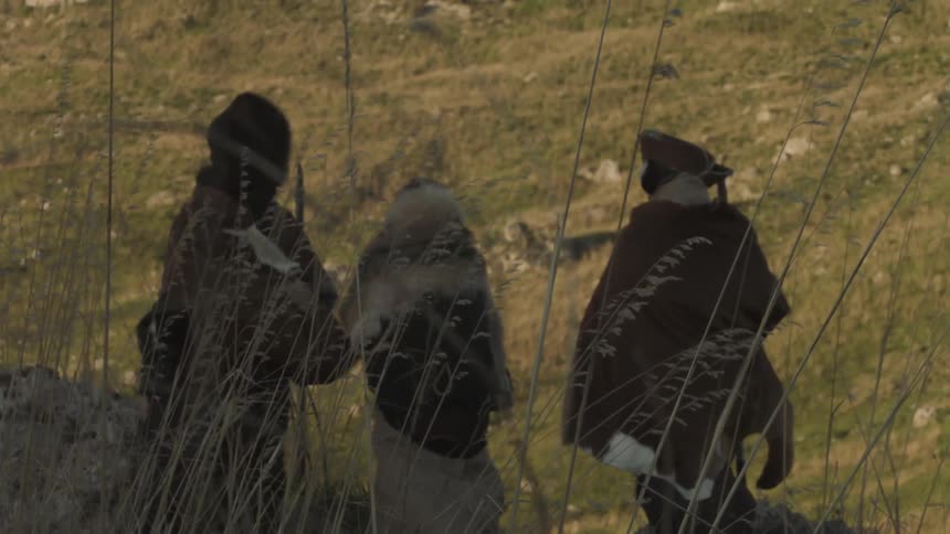 Three men in heavy garments stand near a mountain