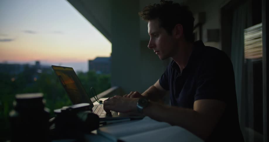 A man is working on his computer on his balcony in the city