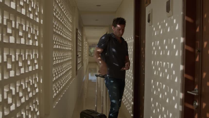 Young photographer carrying luggage on a hotel hallway opens the door to his room