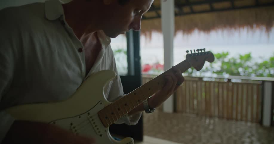 Man strums guitars while sitting in open structure