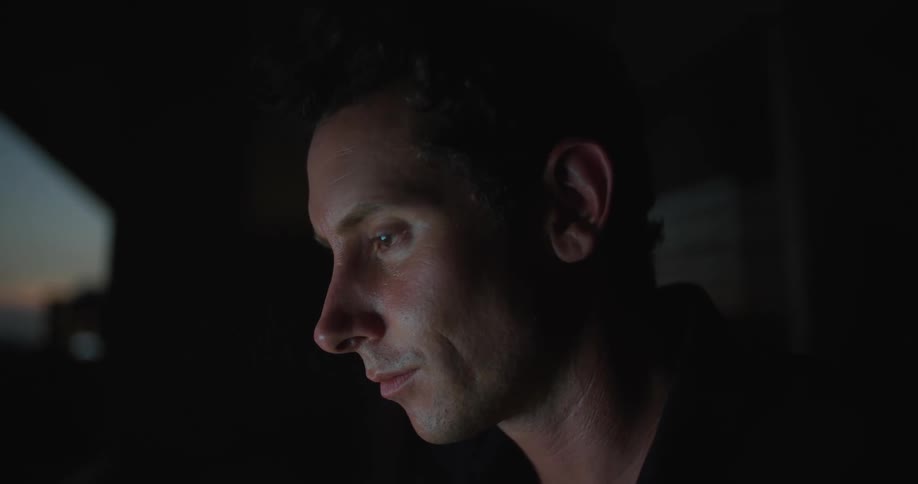 Close up of a man at home thinking while writing on a computer at evening