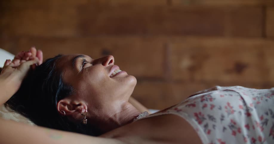 Thoughtful woman lying on bed with arms up smiling