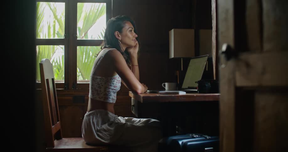 Woman with straight hair earrings printed halter blouse and tattoo types on laptop smiling