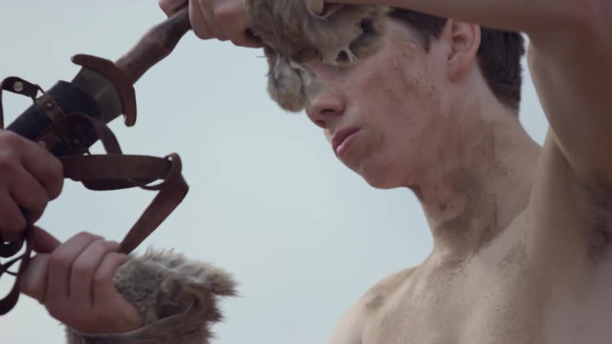 A teenage boy reaches out and pulls a sword partly from a scabbard