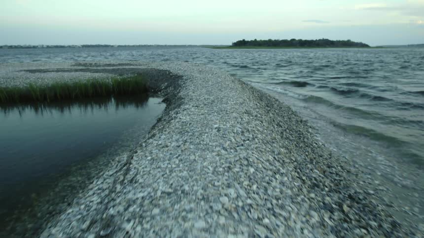 Gathered material of mound forms breakwater across the waves from forest covered land