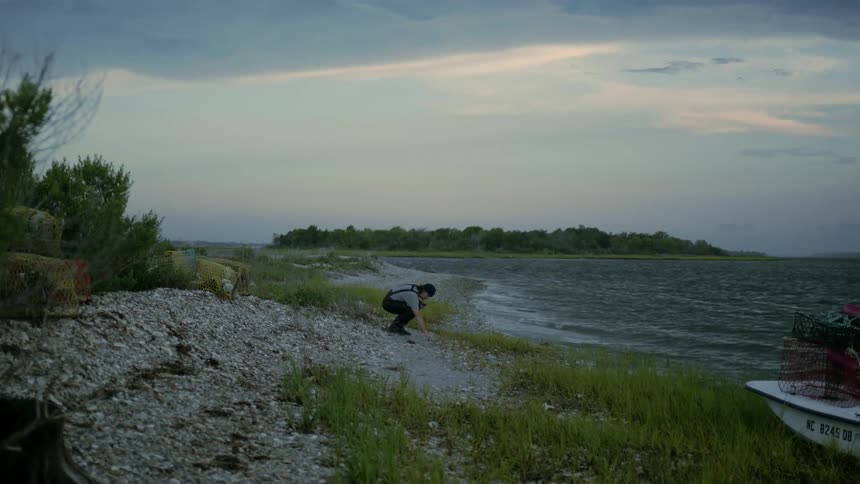 A man standing on a lakeshore on a windy day