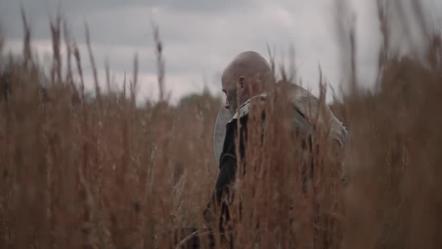 A warrior sitting in tall, dead grass on an overcast day