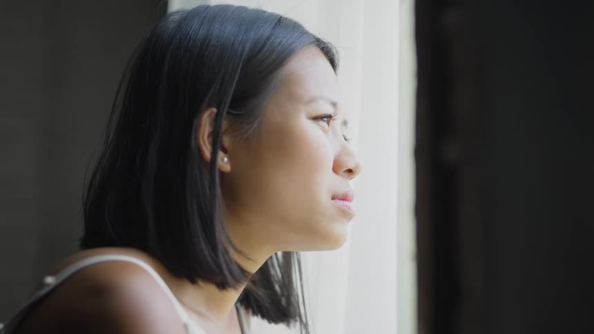 A bored woman looking out a curtained window