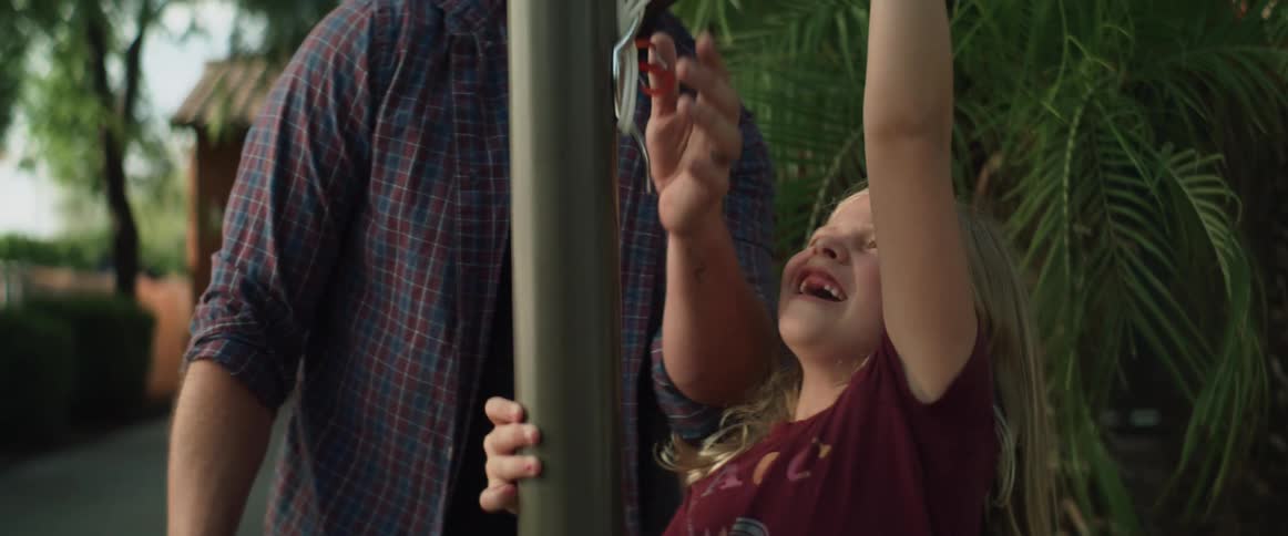 A young girl smiles while helping her father at a flag pole in their yard